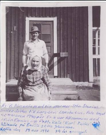 image002.jpg -  Fotograf Erik Almenäs. Bildlån Eriks brorson John Ivar Andersson. Bilden, tagen sommaren 1940, visar Erik med sin mormor Sofia på trappan till Sofias dotter Emelias hus i Oksajärvi. Sofia (Oksa Fia) var född i Lainio 02-05-1852 och dog i Oksajärvi 1940-11-19. Hon var dotter till Emma Kristina Laestadius 1833-07-24-1882-11-20 från Karesuando, dotter till prosten Lars Levi Laestadius, och Johan Jakob Hansson (Oksa Jussa) 1828-12-10-1911-09-06 från Alapäägården i Lainio. De var bosatta först i ett hus vid älvstranden nära nuvarande skolan. Senare byggde de eget hus på Erkontermä strax ovanför huset där Oskar och Inkeri Fredriksson bodde. Det nybyggda huset brann dock ner strax innan Johan med familj skulle flytta in. De fick överta ett hemman i Oksajärvi mot att föregående ägare fick bo kvar i hemmanet så länge han levde. Sofia var född med andra ord i huset vid älvstranden. Sofia hade 2 syskon, Britta Kajsa 1851-01-01-1851-02-02 och Maria Josefina 1854-03-12-1867-07-25 som drunknade i Pajala i samband med konfirmationsläsning där. Sofia gifte sig med Johan Erik Eriksson (Oksa Juhani Erkki) 1841-09-12-1912-11-08 från Erkkogården i Lainio. Johan Erik flyttade till Oksajärvi 1860. Två av Sofias och Johans döttrar gifte sig i Lainio, Amanda (Antun Manda) 1873-06-24-1955-10-18 (Eriks mor) med Anders Henriksson (Kajan Anttu) 1862-09-05-1935-11-16 och Alida (Heikan Alida) 1883-12-05-1956-04-17 med Henrik Henriksson (Henttu) 1859-09-15-1938-04-26 på Heikkagården. Möjligen togs fotot av Alidas son Albin (Heikan Alppini) 1919-05-08-1998-09-03 eller av Karl Andersson 1921-06-06-1991-08-01 (Palon Kalle, hembygdsforskaren) vilka var med Erik till Oksajärvi. Dock hade Erik en kamera med självutlösning. Den funktionen kunde ha även används. (1940 fick man gå till Oksajärvi, 10 år senare kom landsvägen).