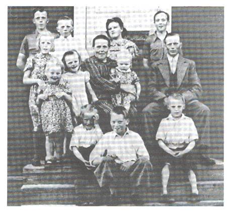 image052.jpg -  Bild från Lainioboken. Foto från 1942. En yngre bror till Hugo bild 51 Oskar Strandelin 1902-1980 övertog Fettogården. Oskar gifte sig med Ida Lasu 1902-1994 från Vivungi. Familjen sitter på trappan på Oskars hemgård. Bakre rad från vänster Hilding 1924-1991, Helge 1928, Frida 1922-1992, Henning 1926 Andra raden från vänster Hanna 1932, framför henne Olivia 1938-194x, Ragnhild 1936, Ida med Majbritt 1940, i famnen, Oskar Nedre raden Ragnar 1936, Hubert 1930, Tage 1934 Sonen Torsten 1942 är ej med på bild, Ann Sofi 1944 var ej född än. Fettohuset ligger på östra sidan älven mitt för skolan på västra sidan.
