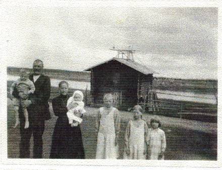 image080.jpg -  Fotograf Karl Johansson Bildlån Natanaels sondotter Berit. f. 1929 boende Risögrund. 1934 var Natanael med hustru Hilma och sonen Karl till Lainio, med följde också Natanaels bror Stefanus hustru Teresia i Malmberget. Natanael som lämnade Lainio 1880 kände inte riktigt igen byn och var hemgården Olla låg. De gick in i Erkkogården och frågade efter var Ollagården låg. Natanaels brorsdotter Mina var ju gift med Oskar på Erkkogården så det blev antagligen fika och dessutom fotografering av familjen Uusitalo. Från vänster Oskar Uusitalo 1878-1944 med sonen Erik f. 1928 i famnen, Vilhelmina (Mina) 1891-1935 med sonen Karl 1930 i famnen, Matilda 1919-2000, Hilda 1922-2006 och Hanna 1925. Bakom landsvägen och aitta som nu är inbyggt i en större byggnad. Bakom älven. 1934 hade Oskar byggt nytt hus. Den gamla Erkkogården var kvar nära nybyggnaden. Mina dog året efter när bilden togs. Av Karl verkar det som om besöket var tidigare än 1934 (1931-32?) Sedan bar det iväg till Ollagården till höger på bilden c:a 700 meter.