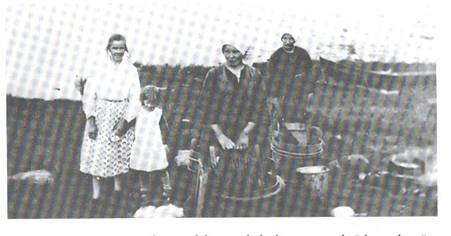 image105.jpg -  Bild från Lainioboken. Början 1930-talet. Här ovan Erkinniva tvättar kvinnorna kläder. Från vänster Julia Elenius 1896-195x med dottern Linnea 1926-199x tittar på, de som tvättar är Hilja Särkimukka 1906-1996 från Kangos och senare gift med Levi Zakrisson. Hiljas morbror var Vaakina Pekka bild 102. Hilja var för tillfället piga på Ollagården. Längst bak Ester Isaksdotter 1906-1998 gift med Valfrid Pudas, senare Fällen, 1907-1983. Närmast älven en båt uppdragen en bit på land. Lainio fick tvättstuga 1954 dit byfolket kunde gå och tvätta till en mindre avgift. Den har all modern maskinell utrustning.