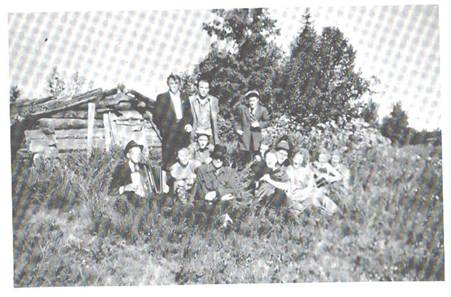 image139.jpg -  Bild från Lainioboken. Från 1940-talet. Slåtterkojan i Saankisaari som fraktades från Angojärvi nära Junojärvi till Saankisaari av Samuel Eriksson och Vilhelm Ylipää. Kojan fanns på en ö i Angojärvi. Ungdomarna brukade staka upp till Saankisaari på midsommarafton. Stående fr. vänster Hilding Strandelin, Carl Andersson, Edvin Uusitalo, senare Valdemar, Hubert Strandelin med dragspel, Karl Uusitalo, senare Nygård, Erik Eriksson med keps, Artur Elenius i hatt, Hanna Strandelin, Ingeborg Eriksson skymtar lite, Märta Eriksson, Ingeborg Eriksson, Gunhild Stålnacke.