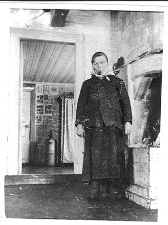 image165.jpg -  Interiörbild Rovagården från 1923. Bild från Lainioboken. Elli Ponga. Elli står vid öppna spisen. Bakom mjölkkammaren med filbunkshyllan. Elli hjälpte pigorna på gården med enklare göromål. När Rovan Poika dog 1927 kom Ellen till lappålderdomshemmet i Jukkas. På gården bodde Temmingi Pirkko, Brita Kajsa 1831-1923 ett tiotal år i slutet av sitt liv liksom Isak Mårtensson (Martin Äjä) 1827-1906. Isaks son Martin Pekka var gift med Rovan Poikas syster Helena. På gamla dagar fick Isak bo hos Rovan Poika.