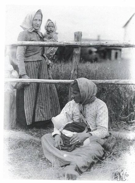 image182.jpg -  Foto Borg Mesch, bild från Drömmen om fjällen av Hans Andersson Vittangi 1912 Sittande kvinnan är Amanda Isaksdotter Pudas 1881-1951 från Näkkälägården i Lainio med sonen Karl f. 1912. Amanda var gift med Isak Arvid Jakobsson 1880-1919 från Klemogården i Lainio, född i Kärendöjärvi och kom som 4 åring till Lainio med föräldrarna. Isak Arvid och Amanda bosatte sig i Vittangi där Isak Arvid var bysnickare vilket även sonen Karl blev. Karl gick ett år i folkskolan i Lainio 1921-22 Stående kvinnan är Isak Arvids syster Maria Karolina Jakobsdotter 1887-1927 gift med Karl Oksajärvi (Oksa Kalle) f. 1877 från Oksajärvi. De bosatte sig i Vittangi i början 1900-talet. Maria har dottern Selma Matilda f. 1912 i famnen. Kvinnorna tar en paus under kornskörden med småbarnen med på arbetet. En av deras söner, Helmer Karlsson 1910-1998, var murare och hade sommarstuga vid färjeläget i Lainio tillsammans med hustrun Engla Vilhelmina Ylipää f. 1918 från Ylipäägården i Lainio.